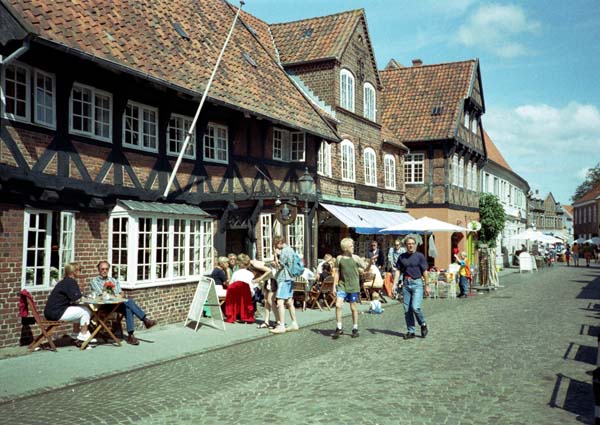 Historic buildings in a street in Ribe, Denmark People walking and sitting on the pavement in a street with old buildings