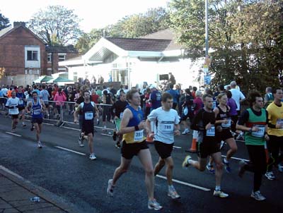 Crowds of runners go along a main road past a white sunlit building