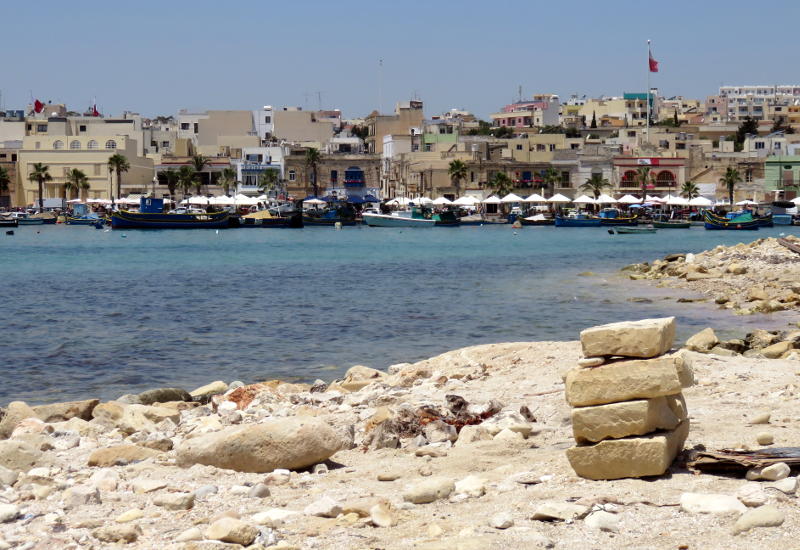 View across a harbour with rocks on a beach in the foreground