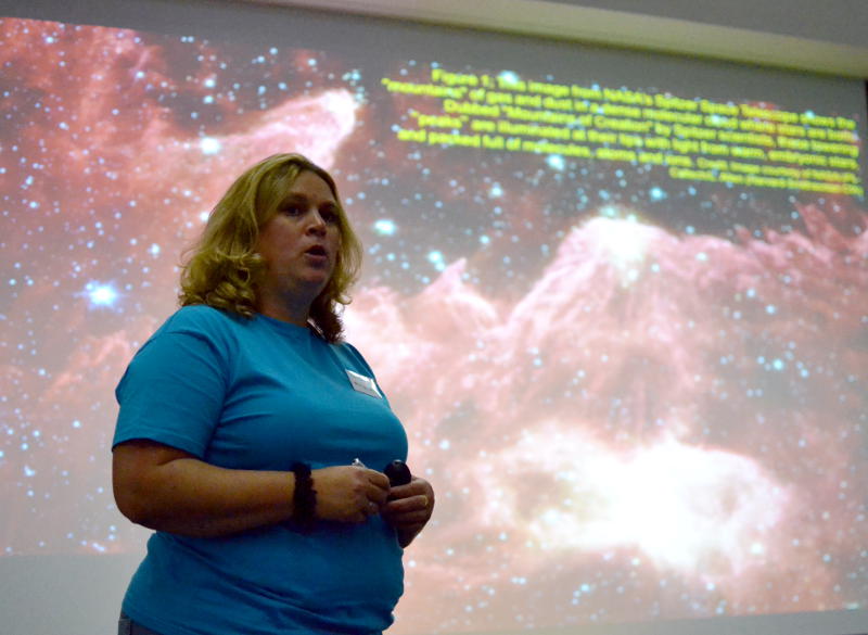 Dr Helen Fraser speaking in front of a screen displaying a nebula