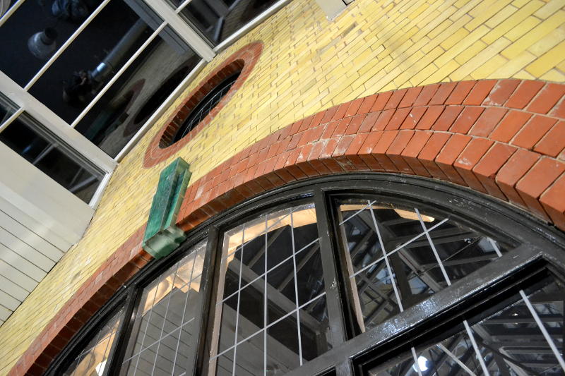 The arch of a window with red and green bricks set into the yellow-coloured wall