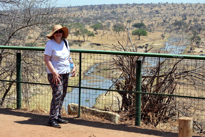 Miriam standing by a metal fence with a river and scrubland in the background