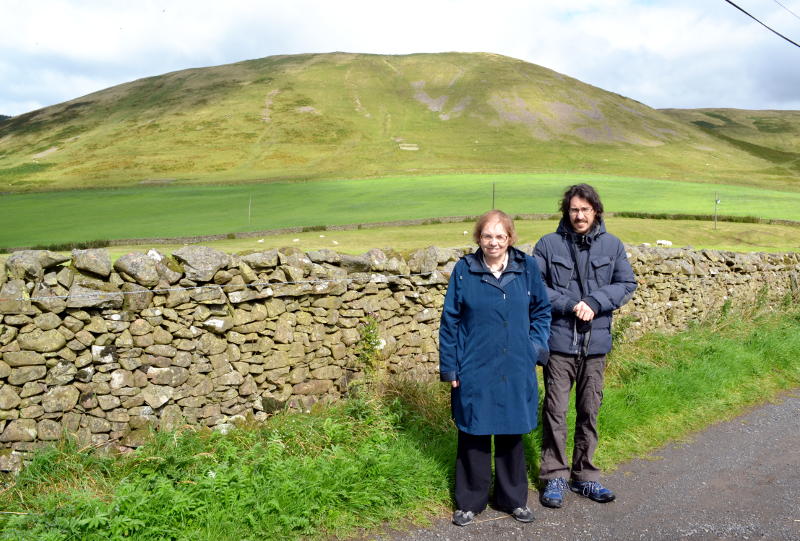 Miriam and Martin standing in front of a dry stone wall with a hill in the background