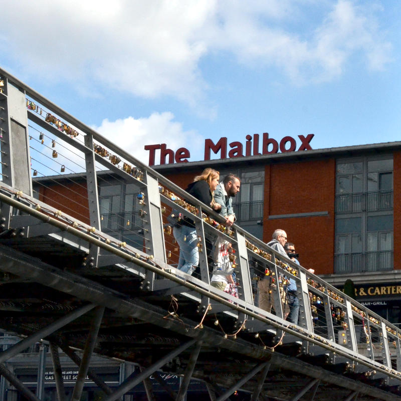 Pedestrians on a footbridge with the Mailbox in the background