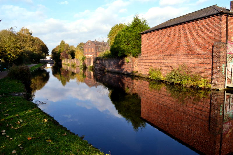 A brick wall and building reflected in the water of the canal