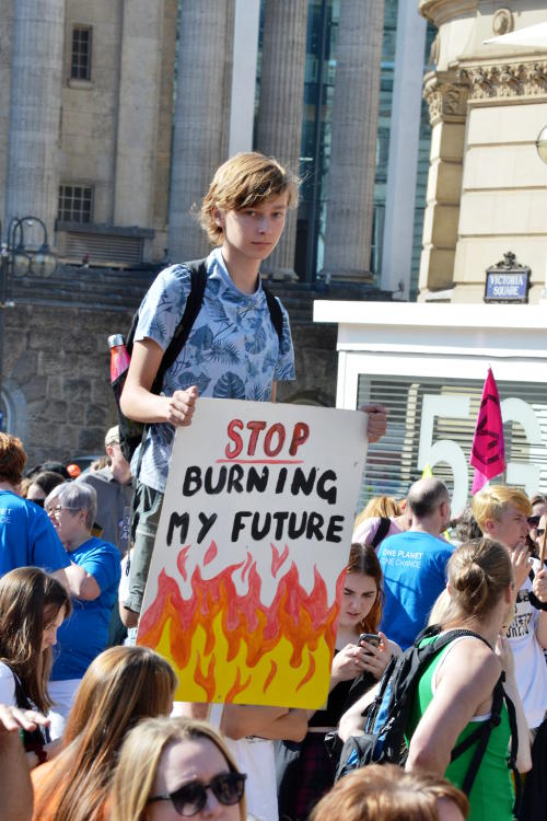 Young man holding a placard: Stop burning my future