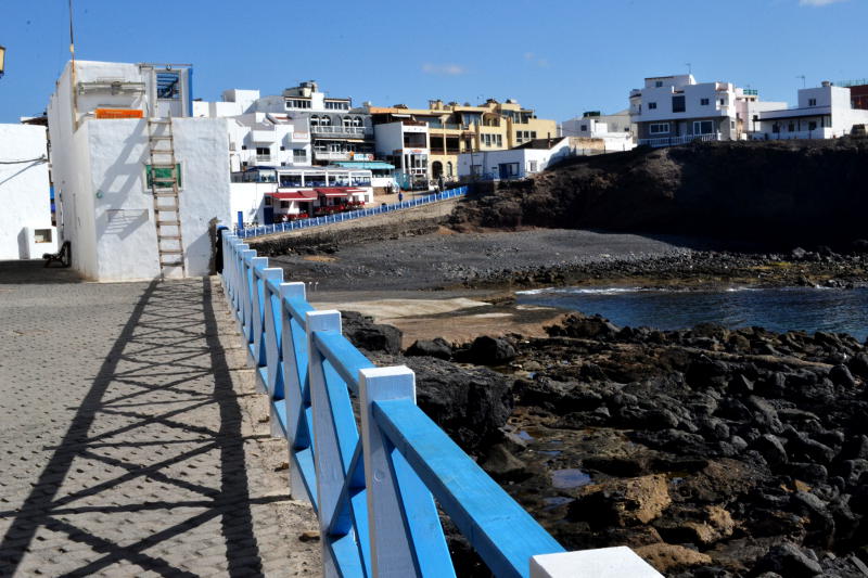 Blue railings around a harbour built of black volcanic rock
