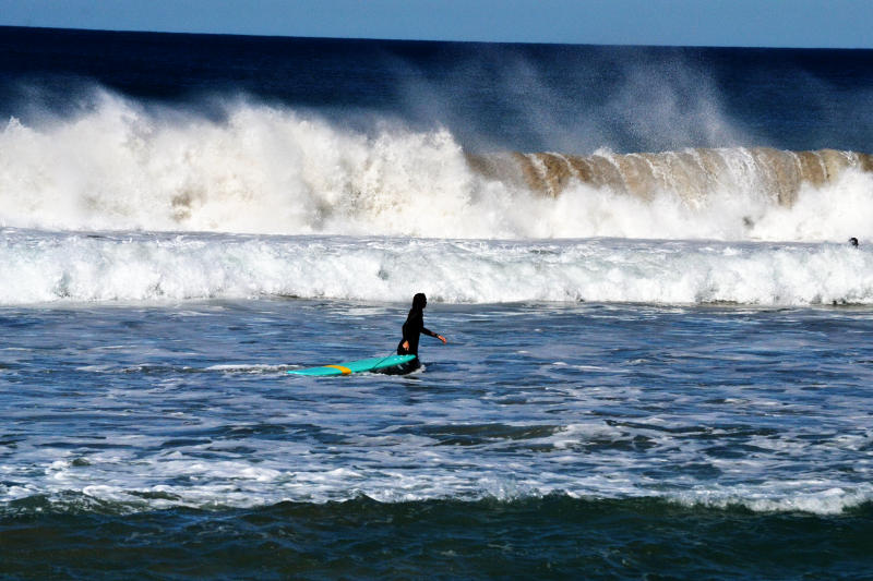 A surfer walking in the sea with a wave approaching