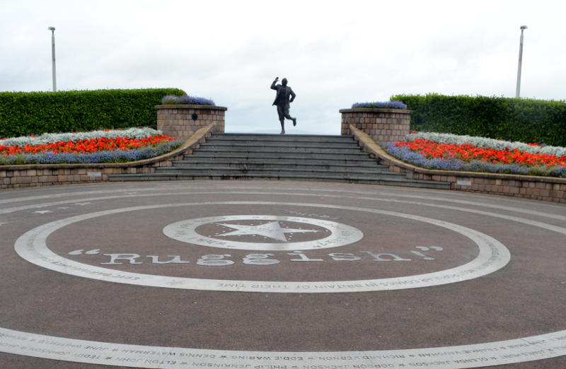 Statue of Eric Morecambe behind a forecourt displaying some of his comic lines
