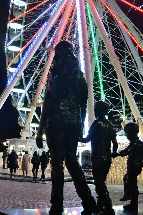 Silhouettes of statues against a brightly-lit Big Wheel