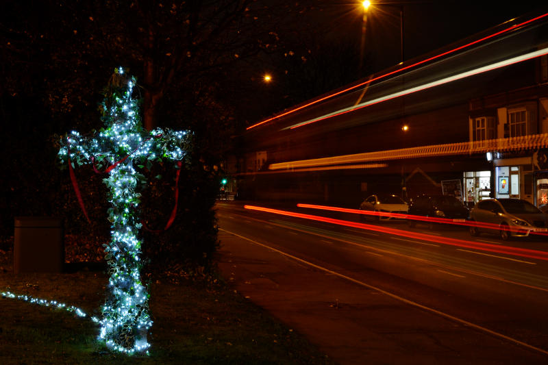 An illuminated cross at night, with light trails from a passing lorry