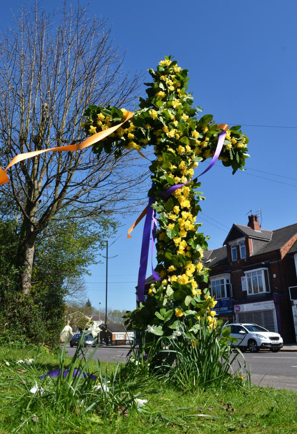 Wooden cross by Pershore Road covered with daffodils