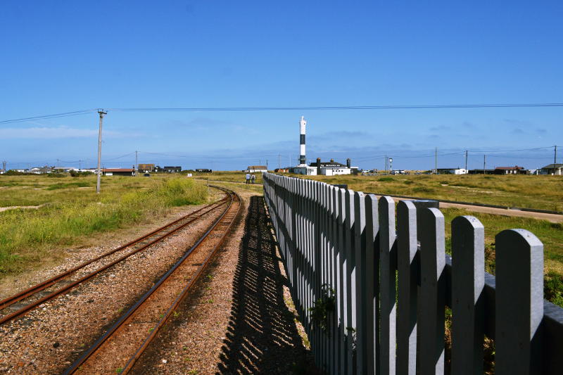 A railway line, wooden fencing and a lighthouse in the distance