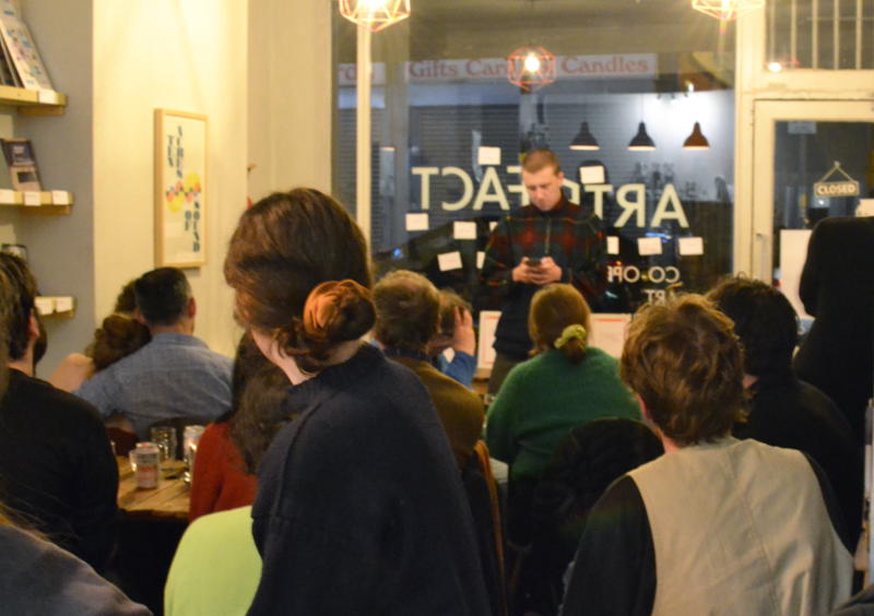 A spoken word performance viewed from the back of the audience