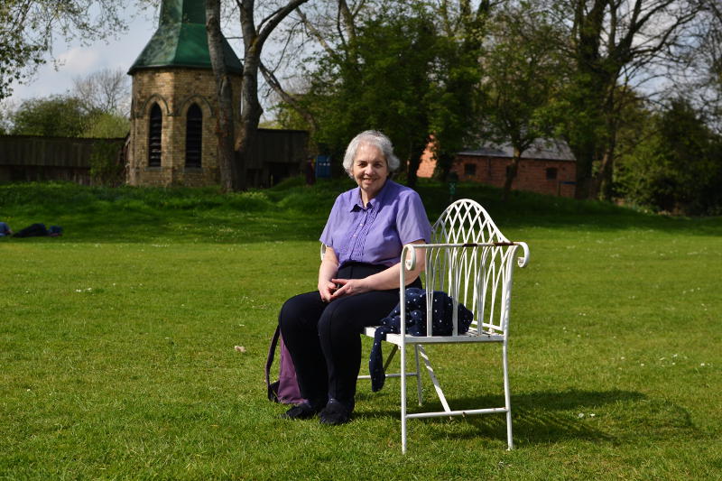 Miriam sitting on an antique-looking metal bench with old buildings in the background