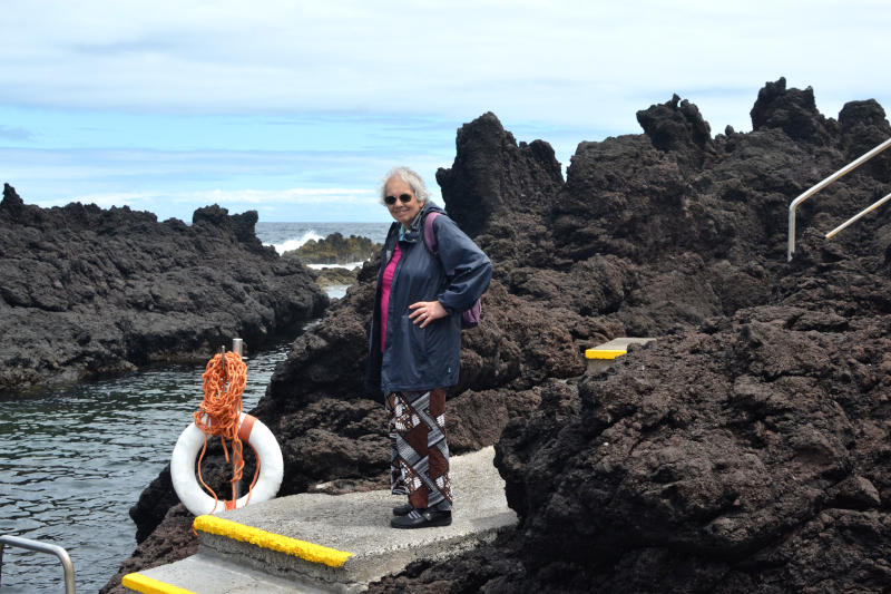 Miriam standing on a concrete platform among lava rocks with the sea in the distance behind
