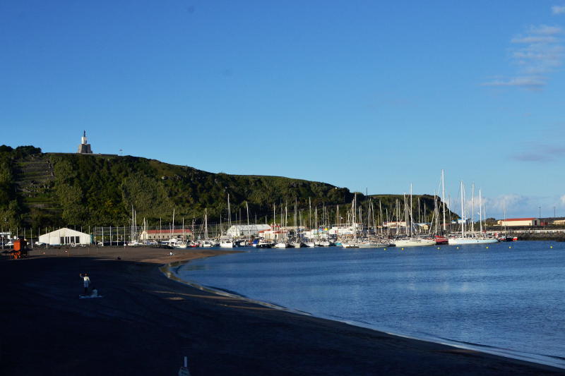 View towards a bay with a yacht harbour and a cliff with a statue on top