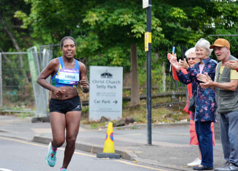 A marathon runner passes Christ Church, to applause from spectators