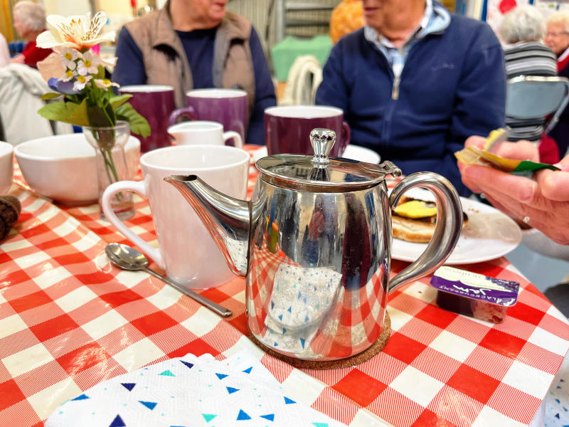 A teapot and crockery on a table with people sitting behind it