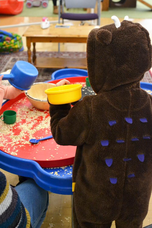 Someone dressed as a gruffalo playing with oats at an indoor sandpit