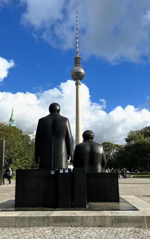 Statues of two seated figures, backs to the camera, facing a TV tower