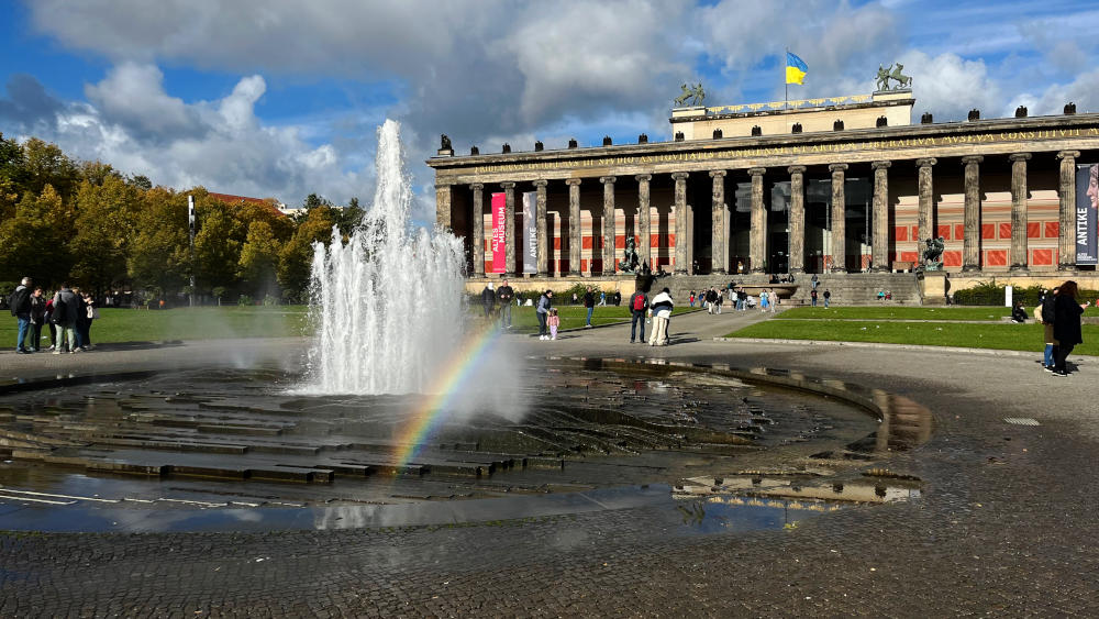 A fountain in an open square with a huge classical-style building in the background