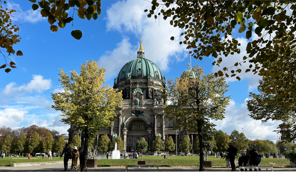 A cathedral with green-topped dome viewed across a grassed open space behind trees