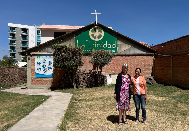 Two women standing in front of a single-storey building with triangular roof and church sign