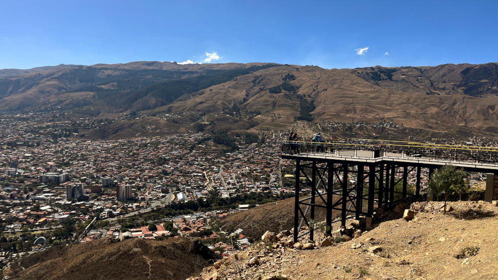 A group of people on a viewing platform overlooking the city spread out below, with mountains in the background