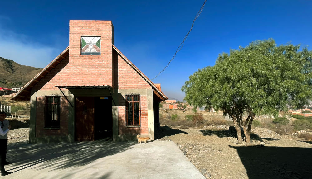 A small brick chapel next to a tree in barren land, in bright sunshine