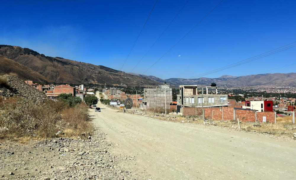 A dusty, unmade road with half built houses alongside it, with mountains in the distance