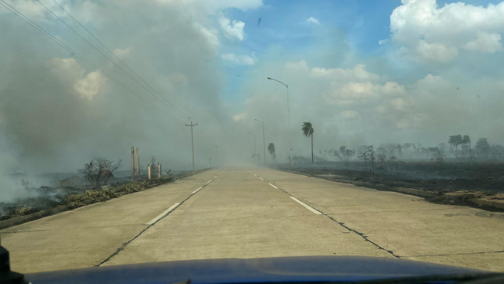 Looking along a road with thick smoke blowing across in the distance