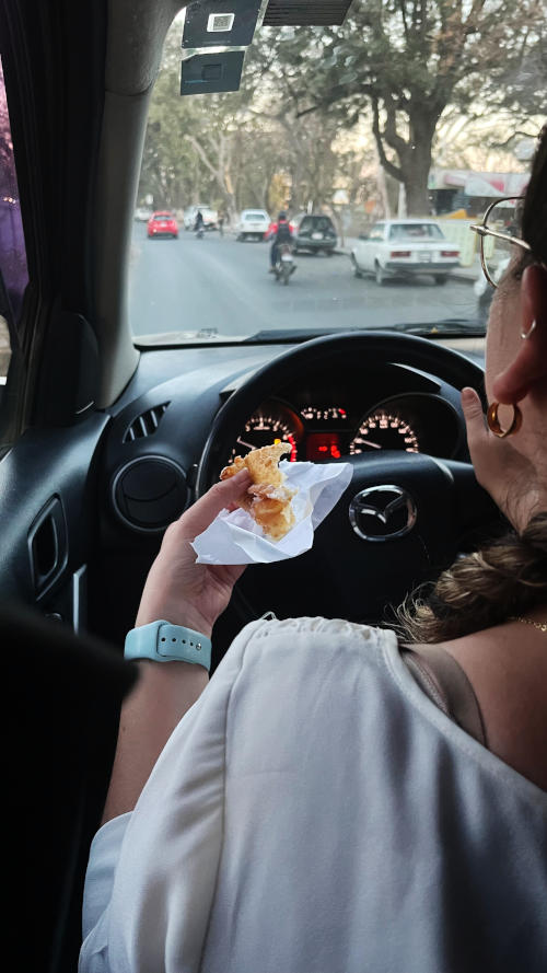 View from the back seat of a car towards the driver who is holding a panuela (food) while driving