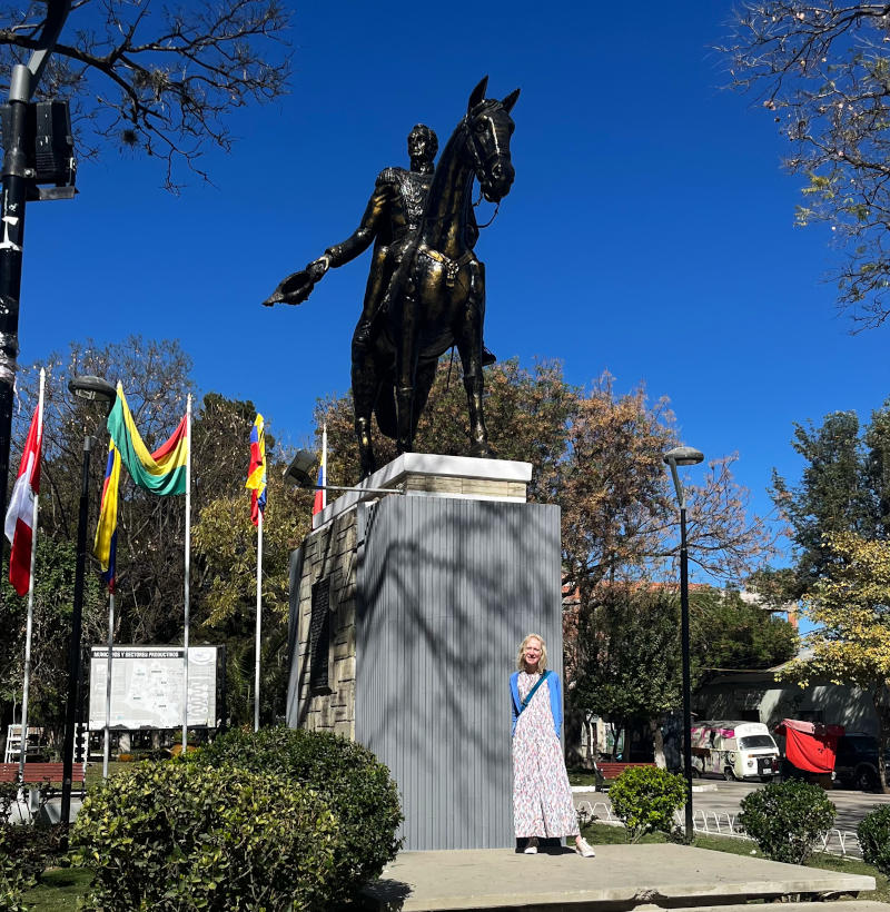 A black statue of a horse and rider on a tall plinth in a park, with a woman standing in front of the plinth