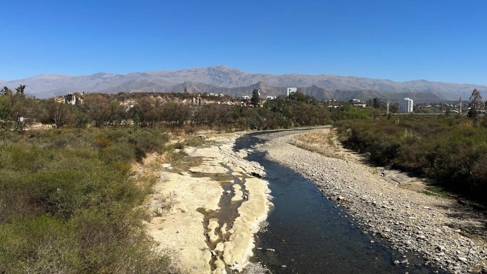 A nearly dried-up river in a wide channel, with mountains in the background