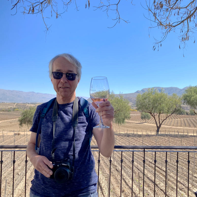 Phil holding a wine glass in front of a barren vineyard with mountains in the distance