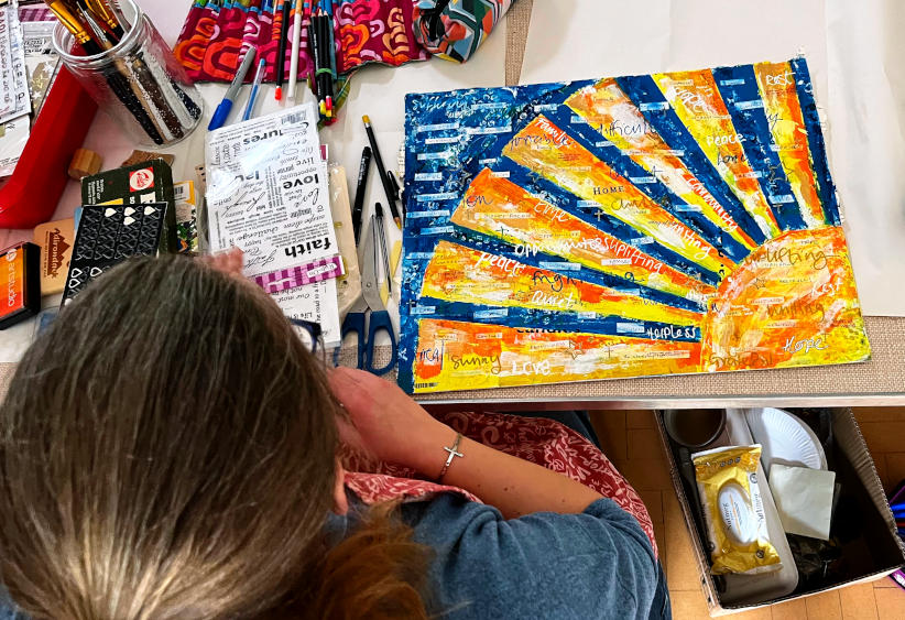 Overhead view of Cheryl creating a piece of artwork: a representation of the sun with light and dark rays emerging and words being stuck on it