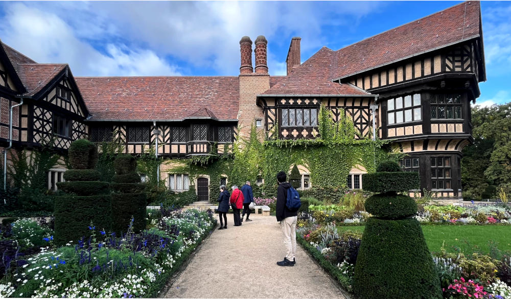 People in a formal garden with a large wood-beamed building in the background