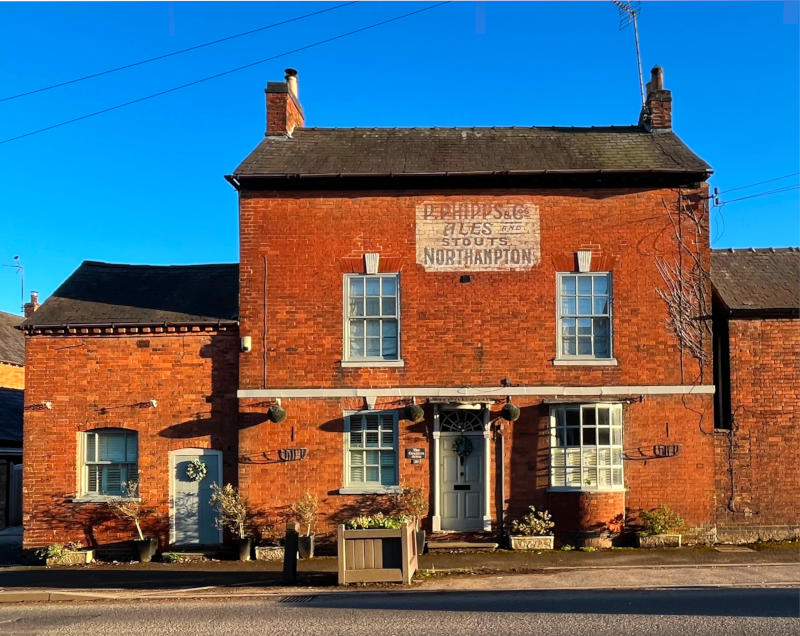 An old redbrick house with "P. Phipps & Co Ales" painted high on the front wall