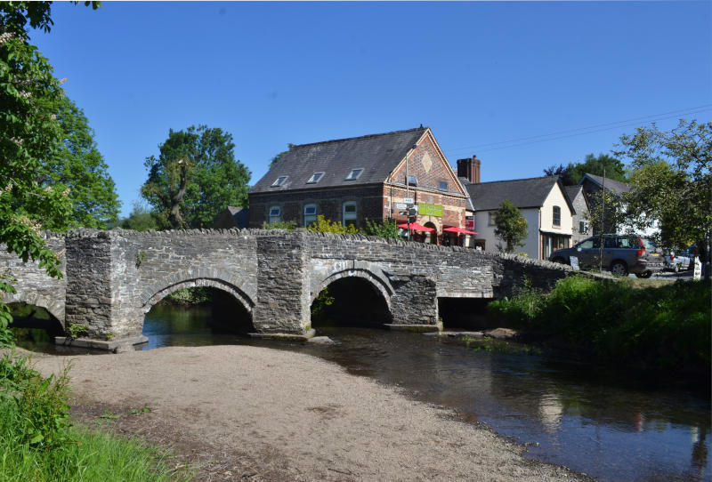 A stone bridge over a river with a café behind