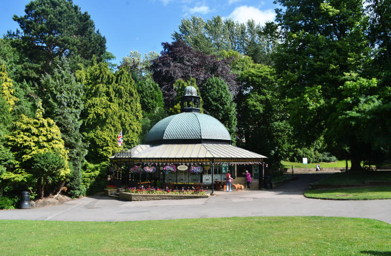 A café in a hexagonal building with a curved roof, in front of multicoloured trees with grass in the foregroun