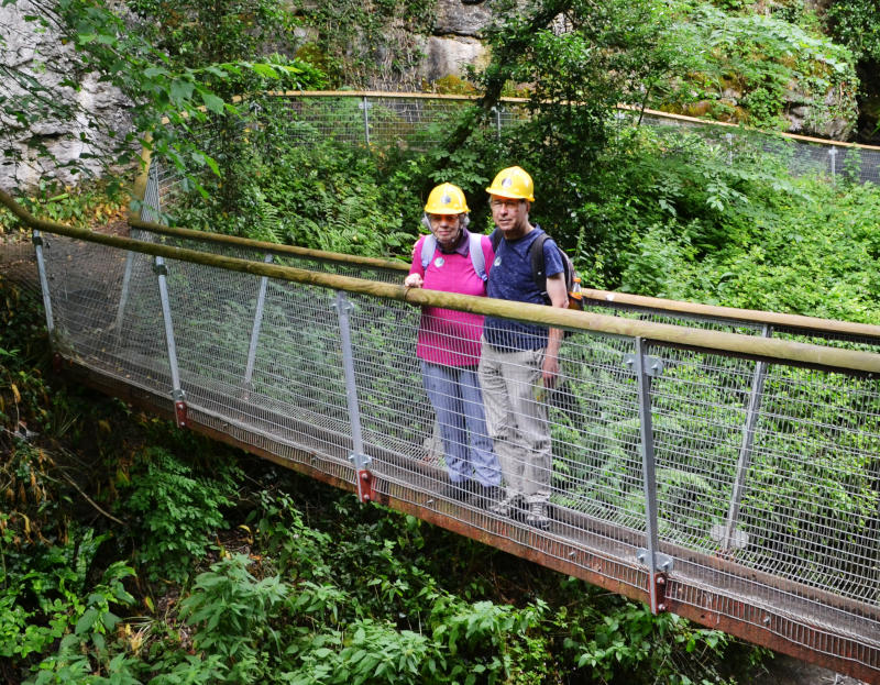 Miriam and Phil wearing hard hats standing on a footbridge in the middle of a narrow gorge
