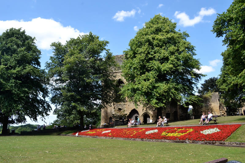 Grass and flowerbeds in front of trees with the ruin of a castle behind