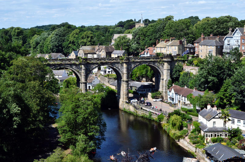 A railway viaduct high up over a river (view from slightly above) and other town buildings behind and below