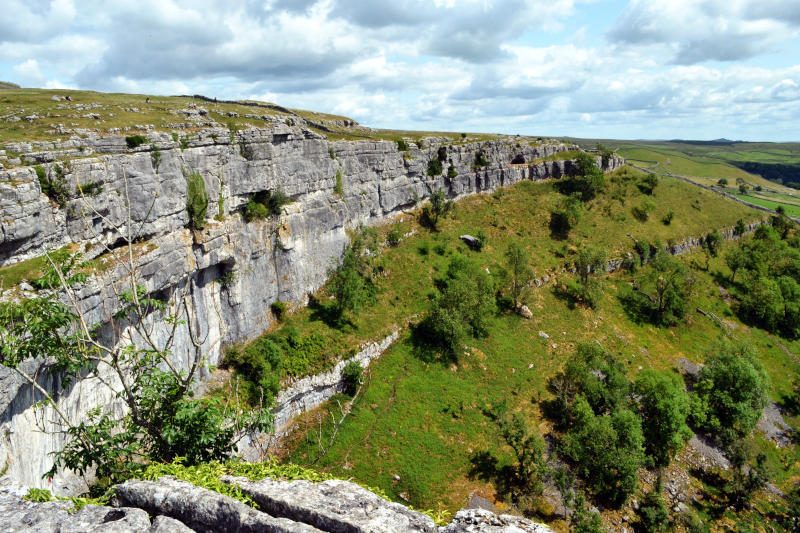 View across a cliff face with grass and trees stretching out below