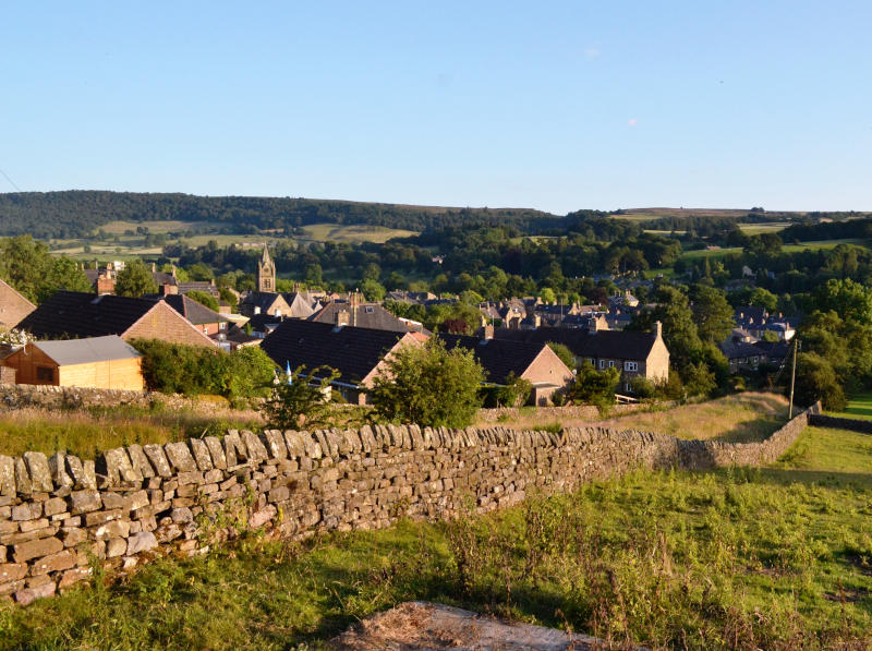 View of the village over a stone wall in evening sunshine, with wooded hills in the background