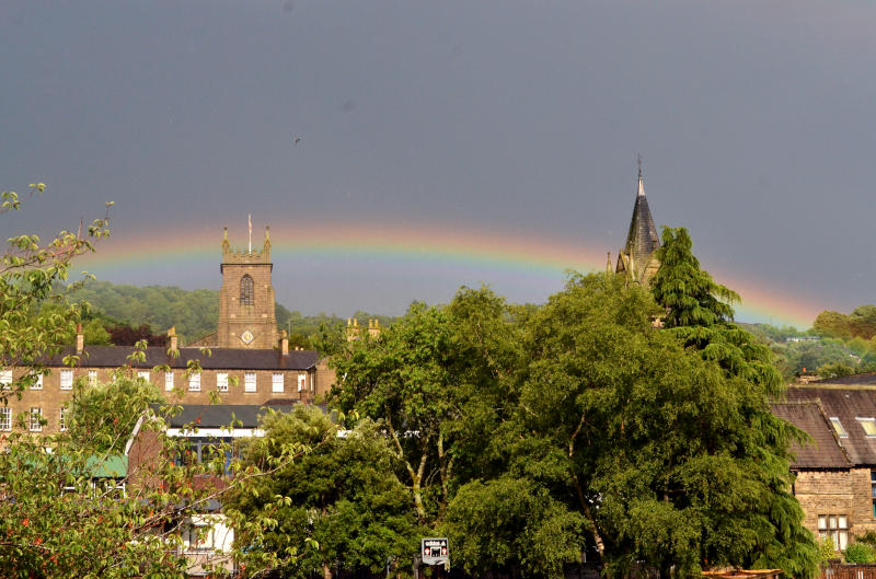 A church tower with trees in the foreground, and a rainbow against a dark sky