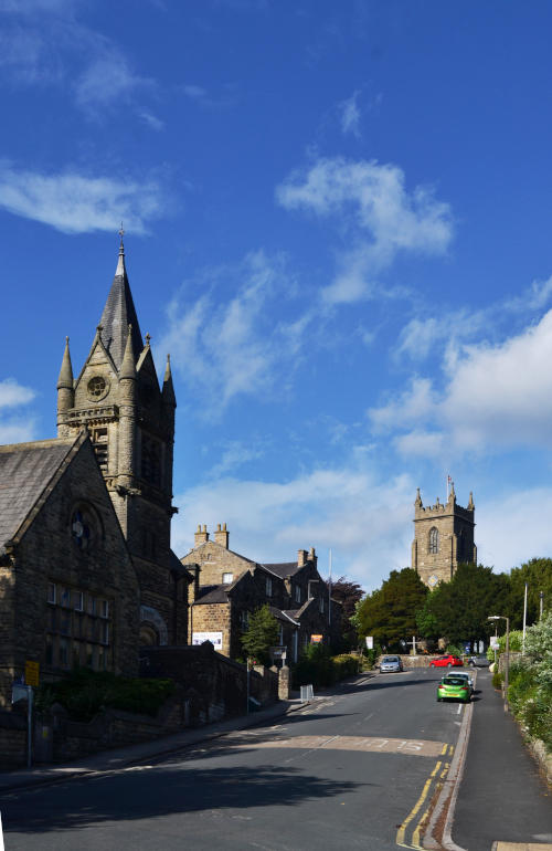 View uphill along a road with a church tower at the top, and a building with a spire on the left
