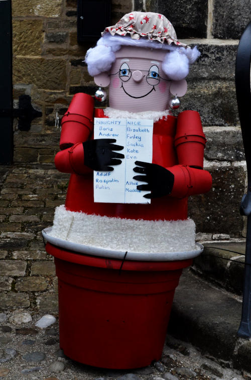 A model of Mrs Goggins (from the Postman Pat series) made out of flower pots, holding a list labelled "naughty" and "nice"