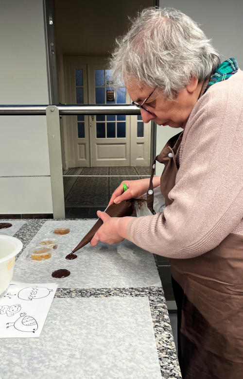 Miriam holding a pipette of molten chocolate which she is squeezing into shapes on a board